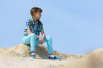 A teenage girl crouched on the top of a mountain and resting examines the surroundings