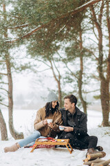 Picnic in the winter pine forest. Lovely couple hugging each others in snowy weather.