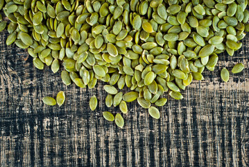 Pumpkin seeds on a black shabby board. Texture of peeled seeds on a wooden table. Copy space and free space for text near nuts.