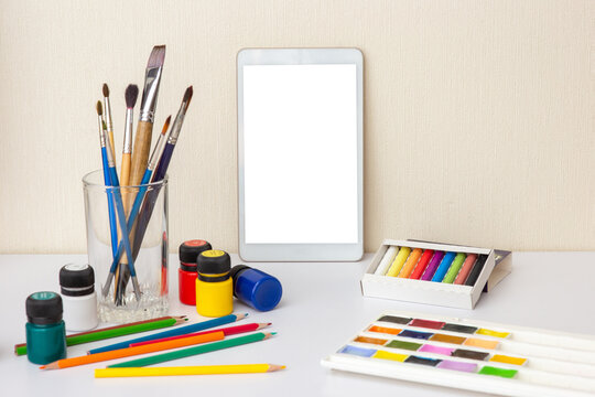 White table with digital tablet with blank screen on white table with colorful drawing supplies