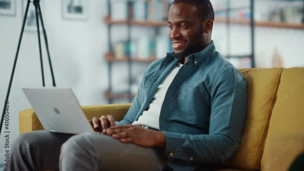 Poster handsome black african american man working on laptop computer while sitting on a sofa in cozy livin