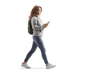 Teenage girl with a backpack walking and typing on a mobile phone