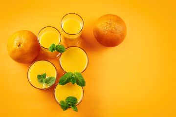 Natural 100% orange juice. Fresh oranges and orange juice in glasses on an orange background. Close up. Copy space.