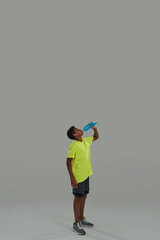 Refreshing after training. Vertical shot of a sporty teenage african boy holding blue energy drink while standing against grey background