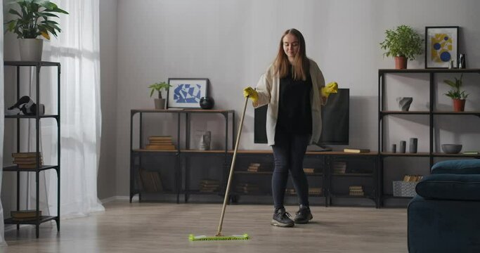 cleaning home at weekend, young woman is washing floor and dancing with mop in apartment, good and joyful mood, help around house