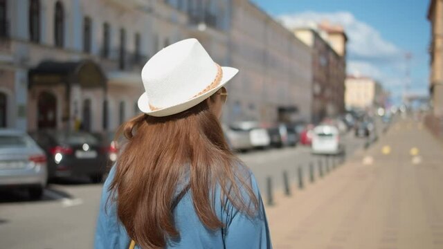 happy woman in hat walking through the city back view, woman walking down the street and smiling