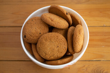 Oatmeal cookies in a white bowl on a wooden background.