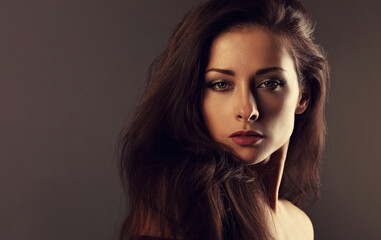 Fototapeta premium Beautiful mysterious woman makeup face and healthy volume brown hair with wisdom emotional look on brown color background with empty copy space. Closeup