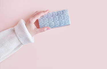 A woman's hand with a manicure in a white sweater on a pink background. Nude gel polish shade, top view, copy space.