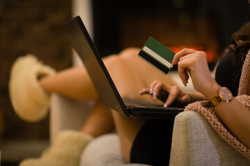 Woman shopping online from home holding credit card and typing on laptop. Female ordering online and relaxing in apartment