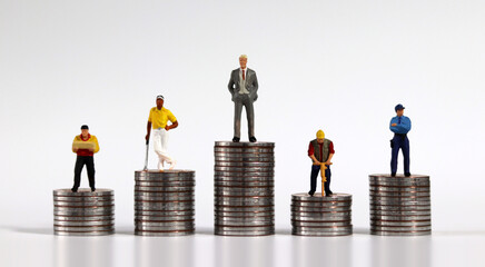 Various miniature people standing on piles of coins of different heights. The concept of economic...