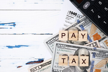 Wooden letters pay tax, personal tax form 1040, dollar bills. Tax payment and filing concept. 