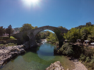 Fototapeta na wymiar Cangas de Onis, Spain - September 4, 2020: The Roman Bridge of Cangas de Onís, the “Puente Vieyu” or “Puentón”. Medieval stone bridge over the Sella River, Asturias, Spain.