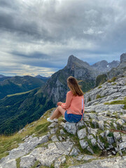 Naklejka na ściany i meble Beautiful young woman sitting next to the Majestic mountains of the Eastern Massif of the Picos de Europa. Eagles flying over Pena Remona.
