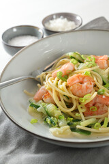 Spaghetti , shrimps, zucchini and spring onions, a healthy Mediterranean meal  in a grey plate with a fork, napkin and spice bowls, vertical  close up shot, selected focus