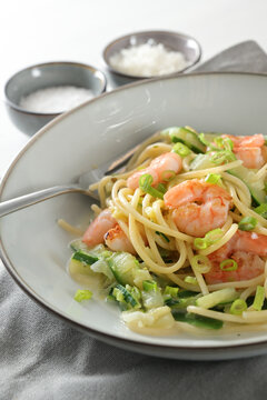 Spaghetti , shrimps, zucchini and spring onions, a healthy Mediterranean meal  in a grey plate with a fork, napkin and spice bowls, vertical  close up shot, selected focus