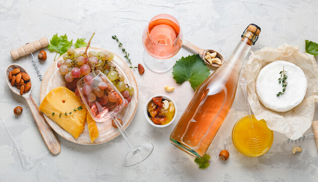 Pink wine rose aged cheese Camembert cheese nuts honey red grapes glasses of wine. Delicious food wine snacks assorted served on boards. Flat lay long web banner on light gray concrete background. - Powered by Adobe