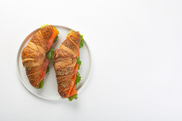 Croissant Sandwich with salmon and salad leaves, top view
