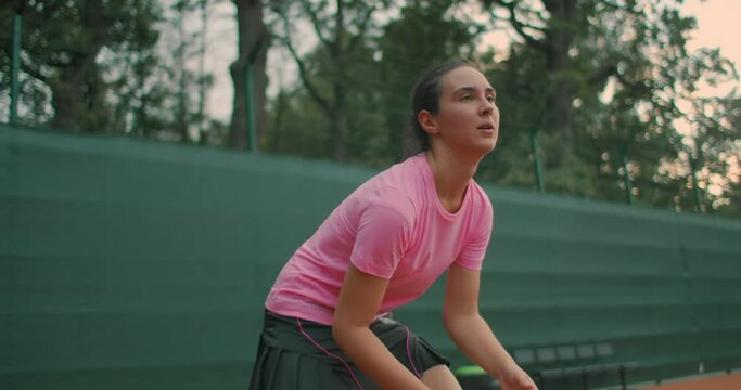 Young tennis player backhand. Young girl in pink t-shirt playing lawn tennis at sunset. Eye Level