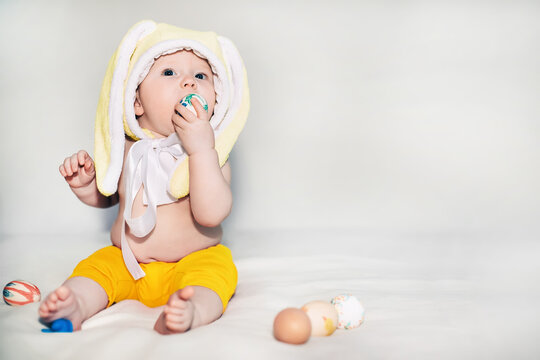 small beautiful baby sitter in yellow illuminate rabbit hat. girl celebrates Easter and found painted decorative egg toy. love and religion concept. Color 2021