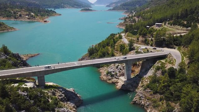 Aerial view of natural landscape with the bridge linking two mountain slopes above sea strait. Clip. Amazing turquoise water of the sea and forested hills. 