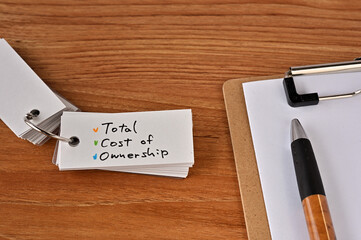 There's a clipboard, a pen and a wordbook stuck to it that says Total Cost of Ownership.