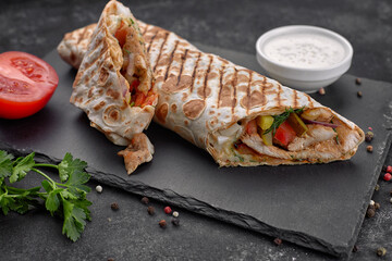 Shawarma with meat, cutaway, with sauce, tomatoes, cheese, herbs and garlic, on black slate, on a black background