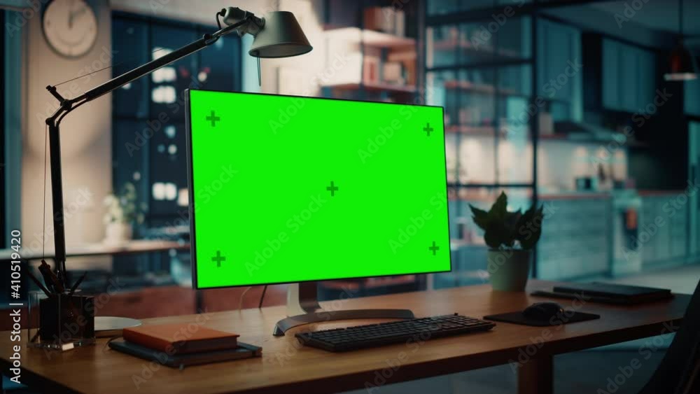 Poster Desktop Computer with Mock-up Green Screen Dsiplay Standing on the Wooden Desk in the Creative Cozy Living Room. In the Background Warm Evening Lighting and Open Space Studio with City Window View.