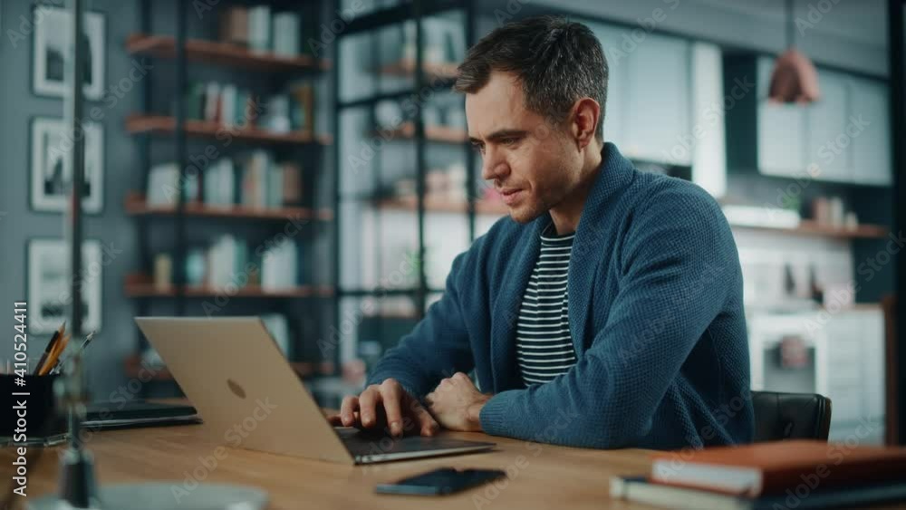 Poster Handsome Caucasian Man Working on Laptop Computer while Sitting Behind Desk in Cozy Living Room. Freelancer Working From Home. Browsing Internet, Using Social Networks, Having Fun in Flat.
