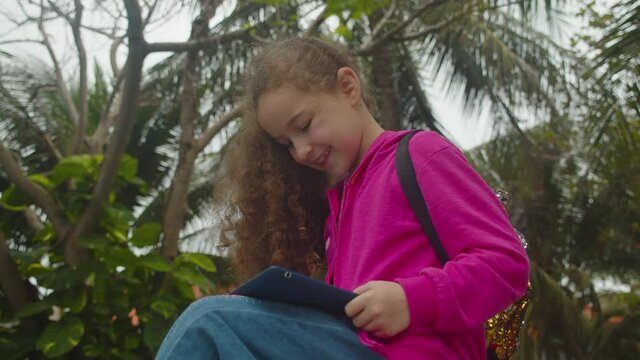 Children tech addiction concept play game. Little Girl Plays in the phone sitting on street alone.