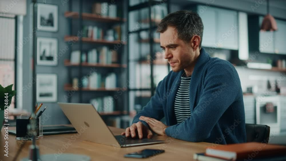 Aufkleber Handsome Caucasian Man Working on Laptop Computer while Sitting Behind Desk in Cozy Living Room. Freelancer Working From Home. Browsing Internet, Using Social Networks, Having Fun in Flat.