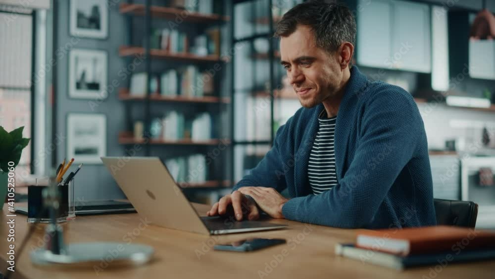 Aufkleber Handsome Caucasian Man Working on Laptop Computer while Sitting Behind Desk in Cozy Living Room. Freelancer Working From Home. Browsing Internet, Using Social Networks, Having Fun in Flat.