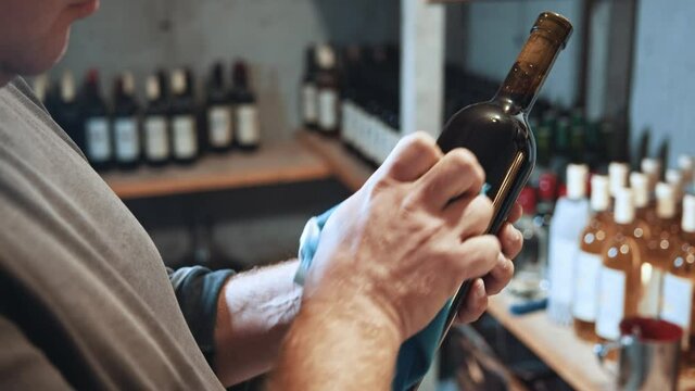 Cropped view of the professional winemaker holding bottle of red wine while wiping it with a cloth from dust before the testing. Working at the wine factory. Winemaking and occupation concept