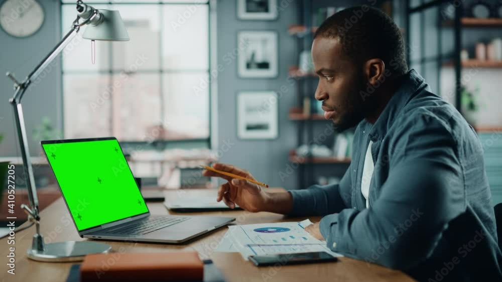 Poster african american man having an online video lesson on laptop computer with mock up green screen in l