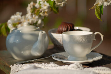 tea set, white tablecloth on a sunny day, cherry blossom branches, marshmallows in chocolate, wooden table. Outdoor breakfast, picnic, brunch, spring mood. Soft focus