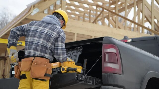 Caucasian Professional Construction Worker and His Wooden Frame of House Contract Job. Staying Next to Pickup Truck Selecting Tools.
