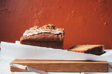 Walnut cake with icing on a wooden board against a burnt orange textured background.