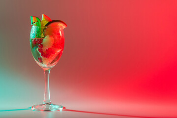 Bright cocktail with fresh fruits in a glass with multi-colored neon lighting. Close-up, copy space.