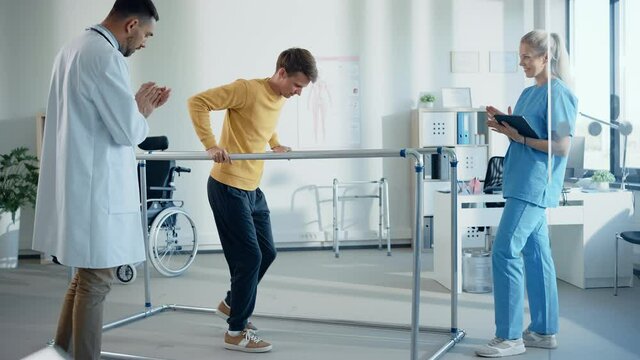 Hospital Physical Therapy: Strong Patient with Back Injury Making First Slow Steps, Walks Holding for Parallel Bars. Physiotherapist, Rehabilitation Doctor Assist, Help, Encourage Disabled Person