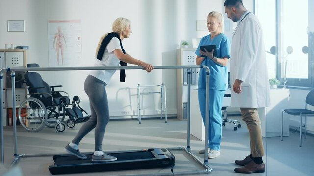 Hospital Physical Therapy: Strong Determined Senior Female Disabled Patient with Injury Walks on Treadmill Holding Parallel Bars. Physiotherapist, Rehabilitation Doctor Assist, Help Disabled Person