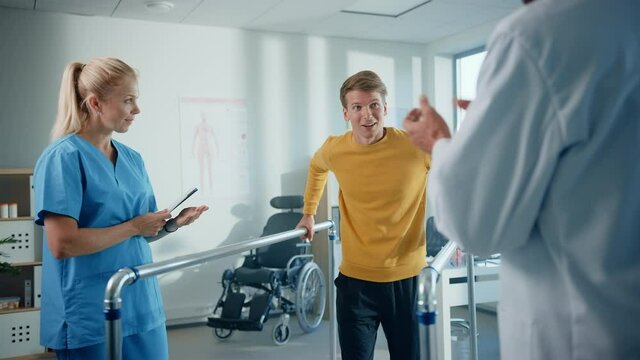 Hospital Physical Therapy: Strong Determined Male Patient with Injury Successfully Walks Holding Parallel Bars. Physiotherapist, Rehabilitation Doctor, Help, Assist, Encourage Disabled Person to Heal