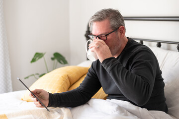 Fototapeta premium Man drinking coffee and reading a tablet in bed