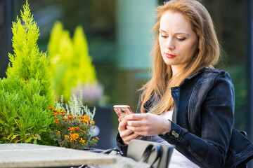 Woman wait in outdoor cafe, looking at cell phone