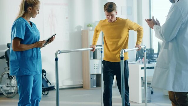 Hospital Physical Therapy: Male Patient with Injury Successfully Walks Holding Parallel Bars. Physiotherapist, Rehabilitation Doctor, Help, Assist, Disabled Person. Elevating Slow Motion