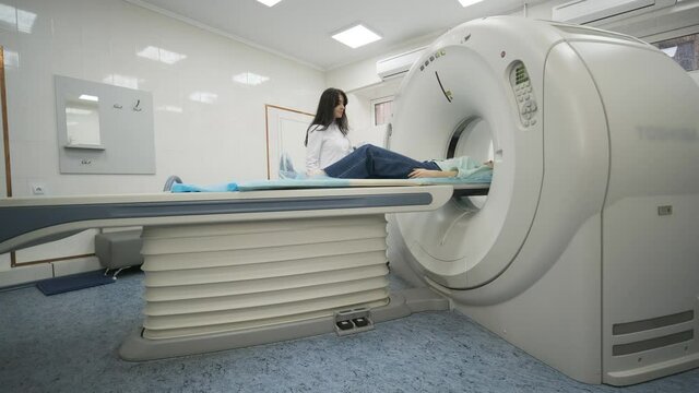 Female patient is undergoing CT or MRI scan under supervision of a radiologist in modern medical clinic. Patient lying on a CT or MRI scan bed, moving outside the machine.