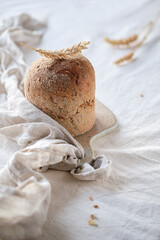Dinkelbrot in German that means spelt. Loaf of wholemeal dinkel rye bread. Dinkel or Spelt is an ancient grain, alternative to wheat. Off white, ivory textile tablecloth, wheat ear decorations.