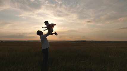 Dad tosses his happy daughter into blue sky. Daddy and a small child play together on field, laugh and hug. Family travel. Child is in arms of parent. Father day off. Happy family and childhood