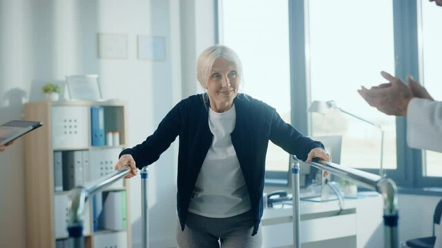 Hospital Physical Therapy: Portrait of Strong Senior Female Patient with Injury Successfully Walks Holding Parallel Bars. Physiotherapist, Rehabilitation Doctor, Help, Assist Disabled Patient