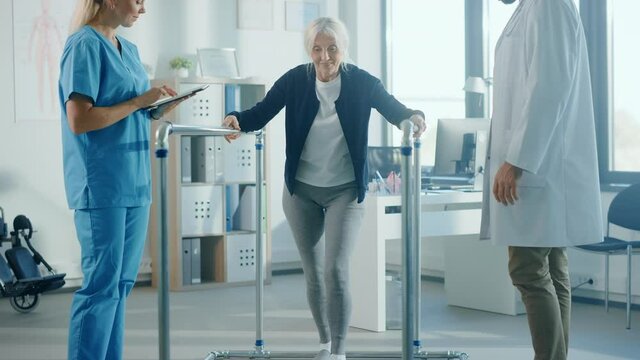 Hospital Physical Therapy: Portrait of Strong Senior Female Patient with Injury Successfully Walks Holding Parallel Bars. Physiotherapist, Rehabilitation Doctor, Help, Assist Disabled Patient