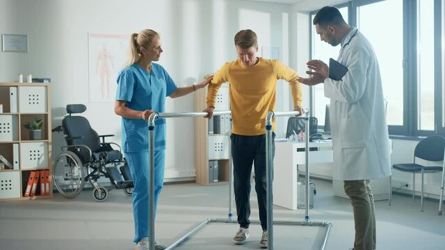 Hospital Physical Therapy: Portrait of Strong Young Male Patient with Injury Successfully Walks Holding Parallel Bars. Physiotherapist, Rehabilitation Doctor, Help, Assist, Disabled Person